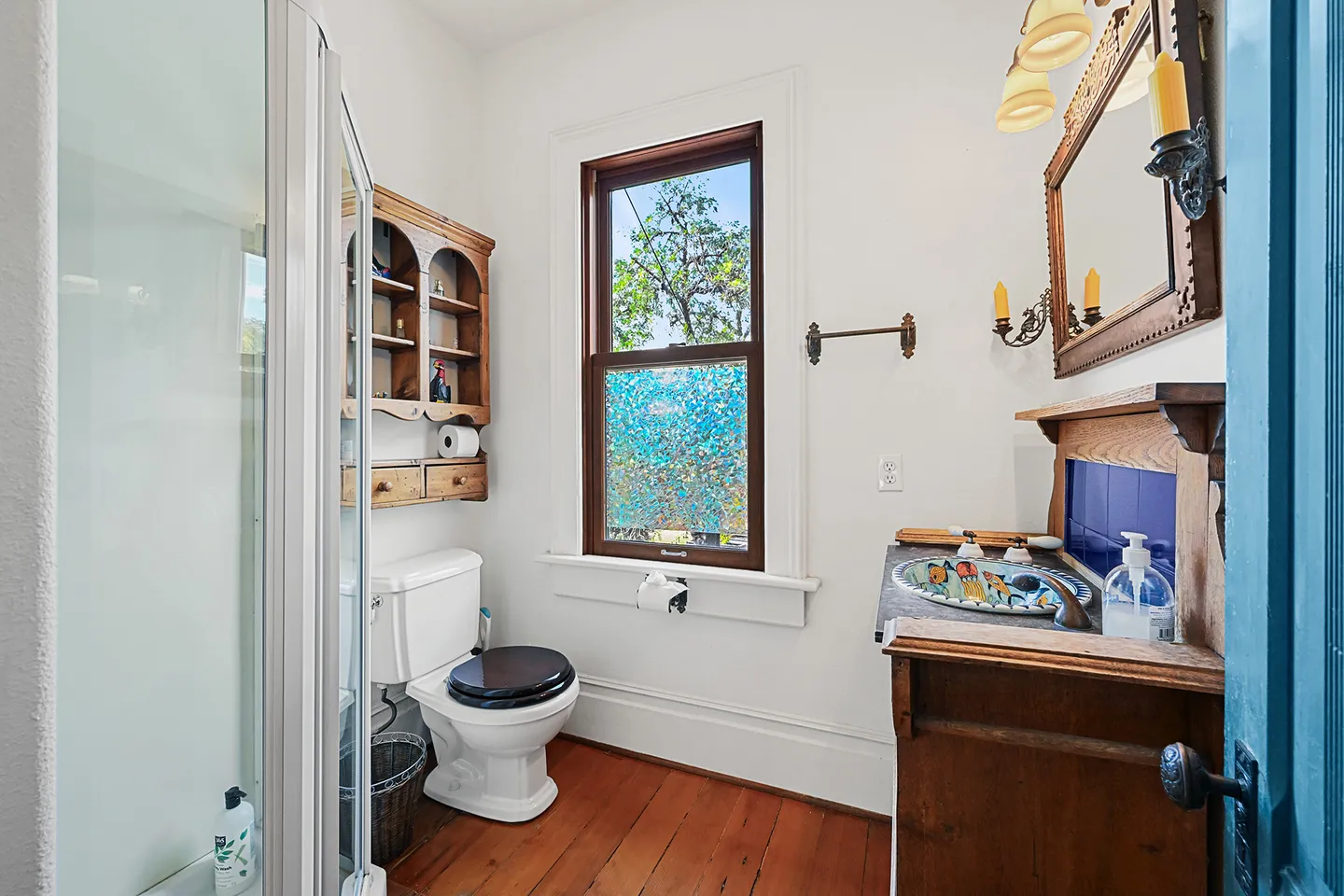 Bathroom featuring a glass-enclosed shower, toilet, wooden vanity with a colorful vessel sink, and wood floors.