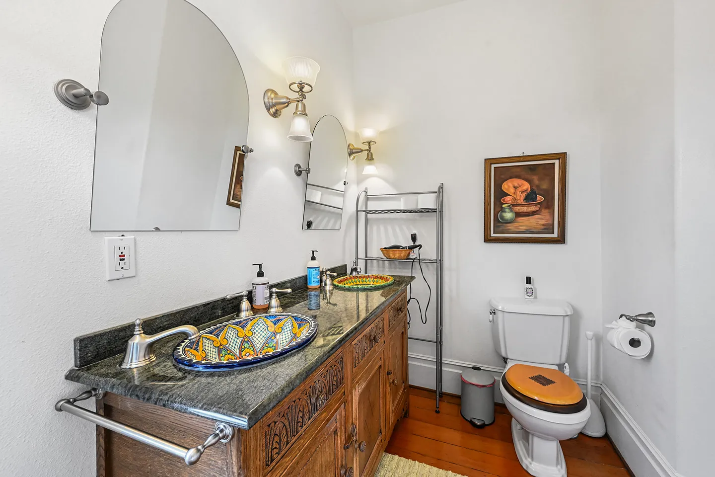 Bathroom with a double vanity featuring ornate wooden cabinetry, colorful hand-painted sink basins, dual arched mirrors, and a toilet in the corner.