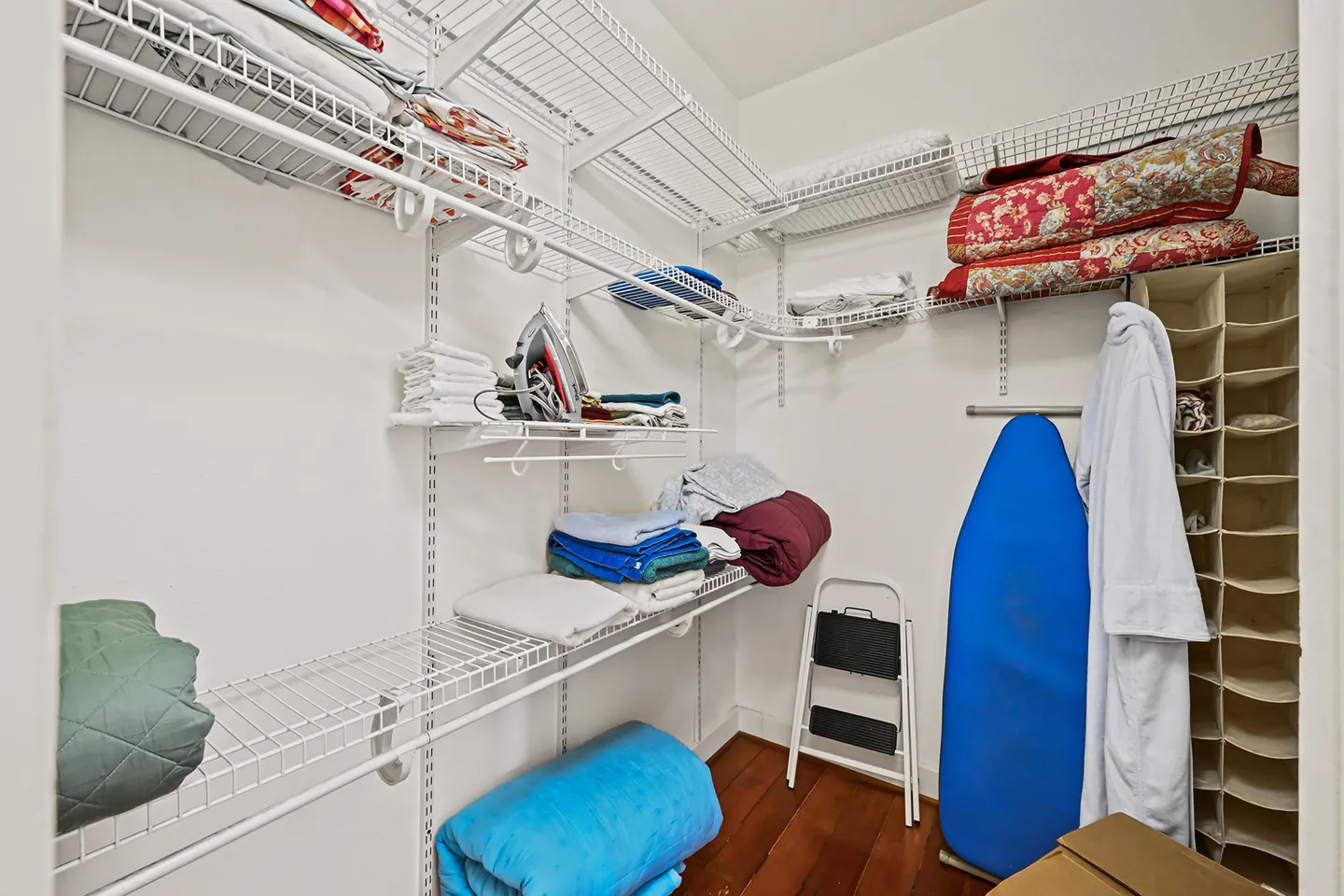 Walk-in closet with white wire shelving holding folded linens, an iron, an ironing board, and a robe.