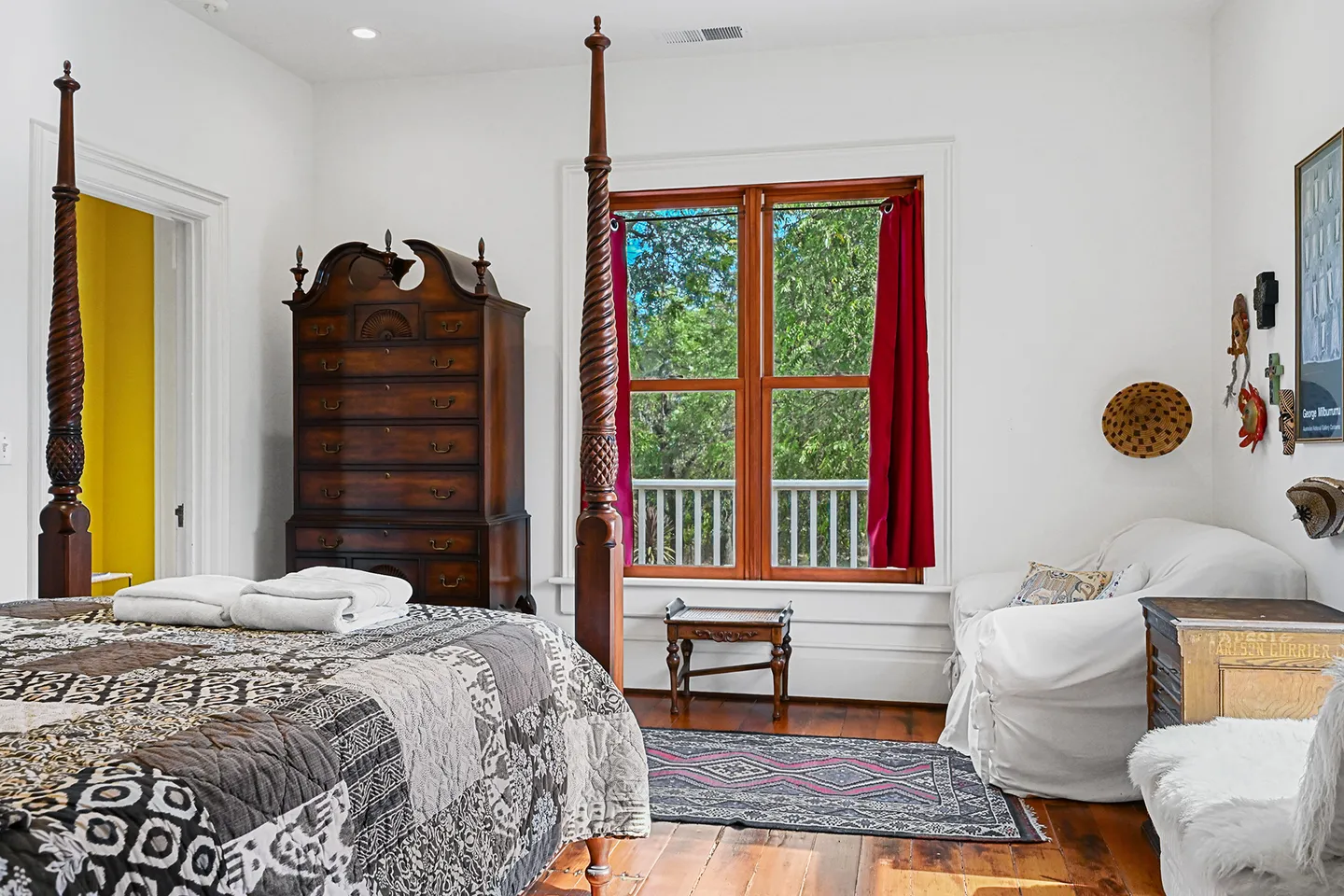Bedroom featuring a carved wood four-poster bed, a tall wooden chest of drawers, and a window with views of green trees and a porch railing.