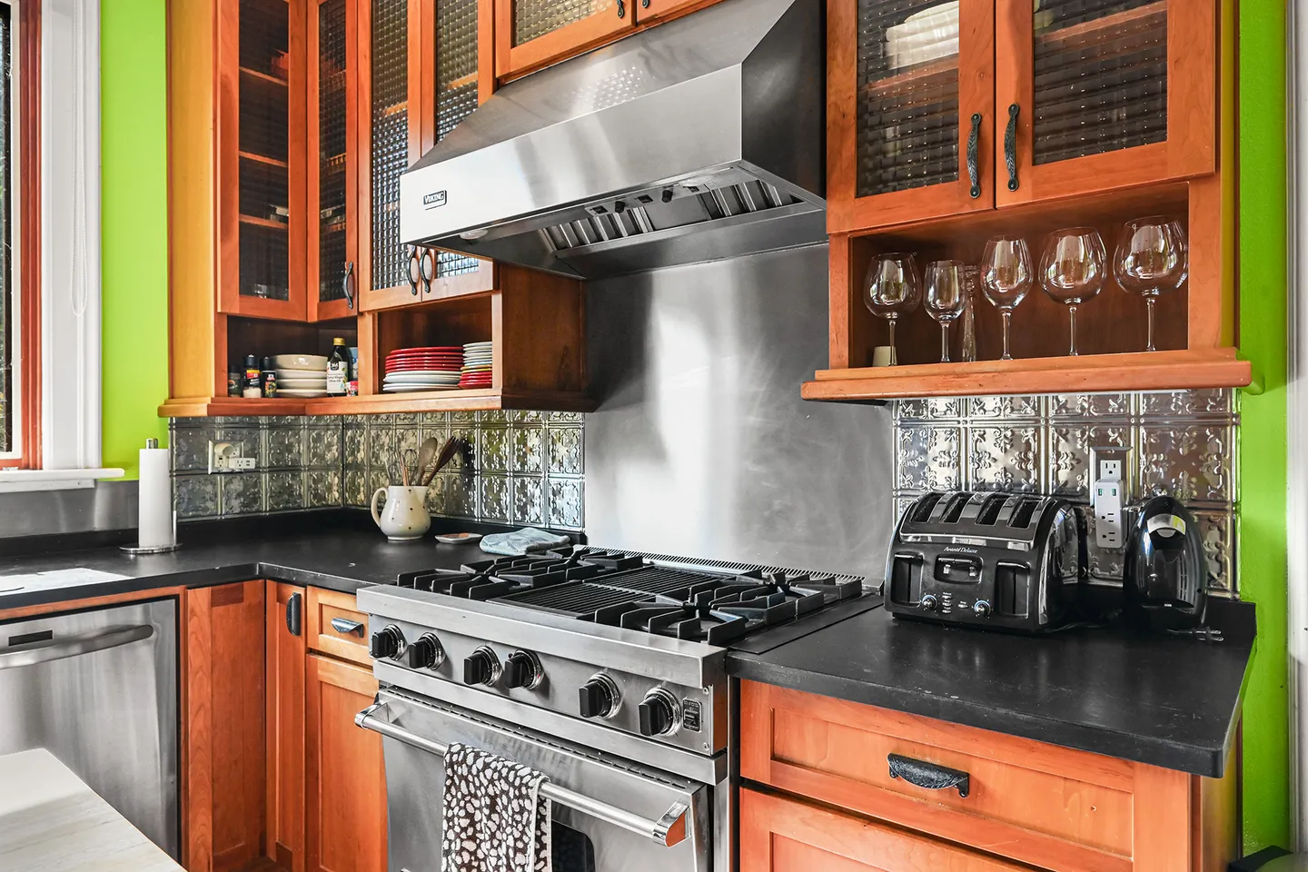 Kitchen counter area featuring a stainless steel Viking gas range and range hood framed by wood cabinets and a pressed-tin backsplash.