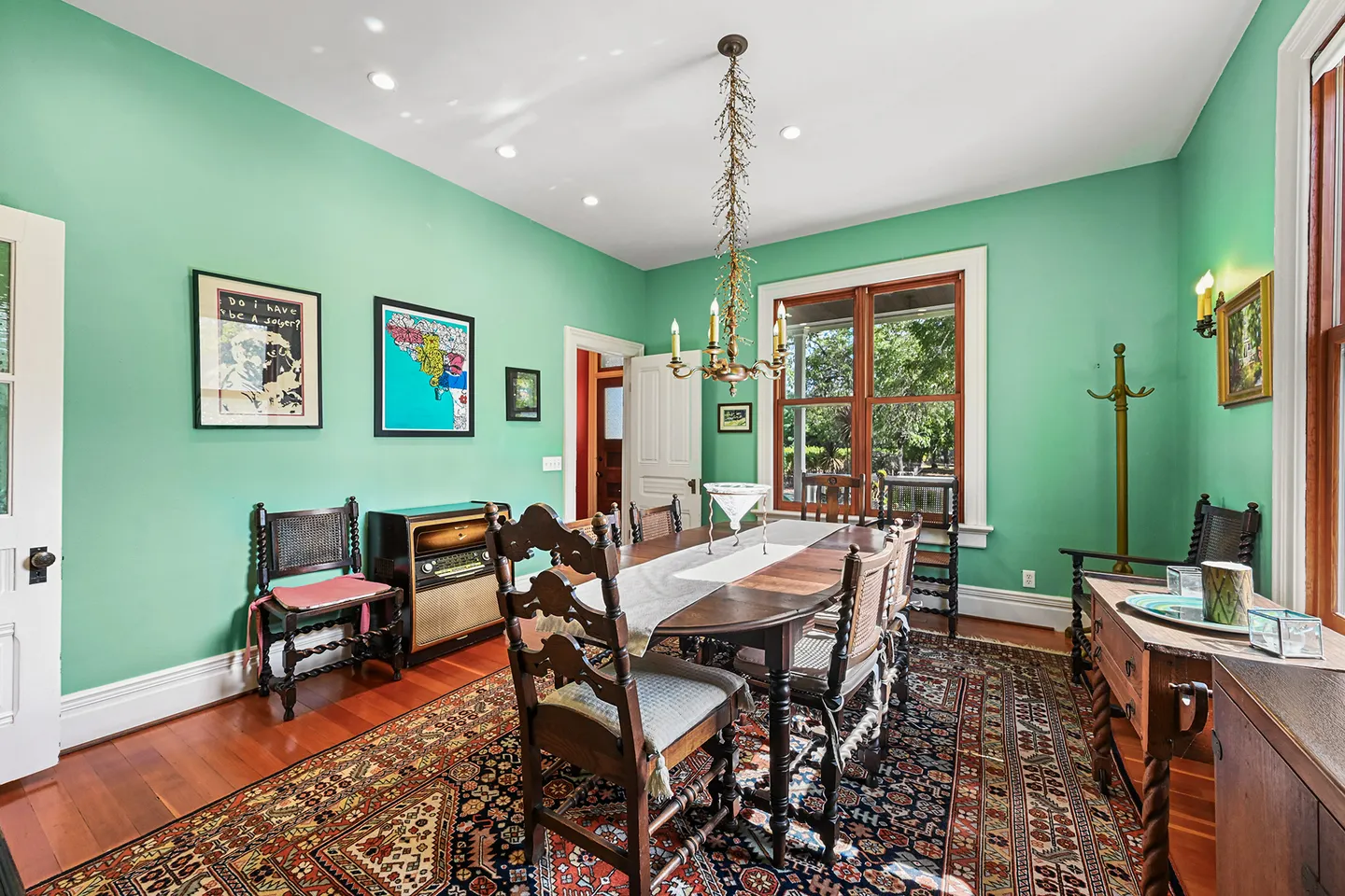 Dining room with mint green walls, wood dining table with chairs, an ornate area rug, and hardwood flooring.