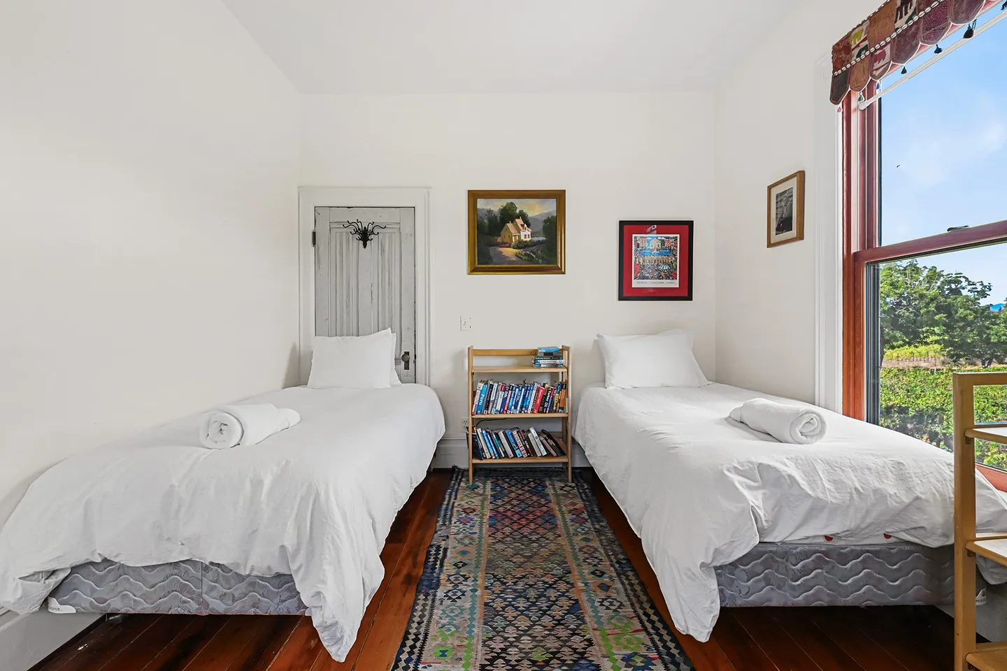 Bedroom with two twin beds made up with white linens separated by a patterned runner rug and a small bookshelf.