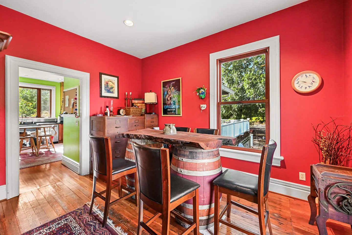 Dining area with bold red walls, hardwood floors, and a live-edge table supported by wooden barrels with high-back chairs.