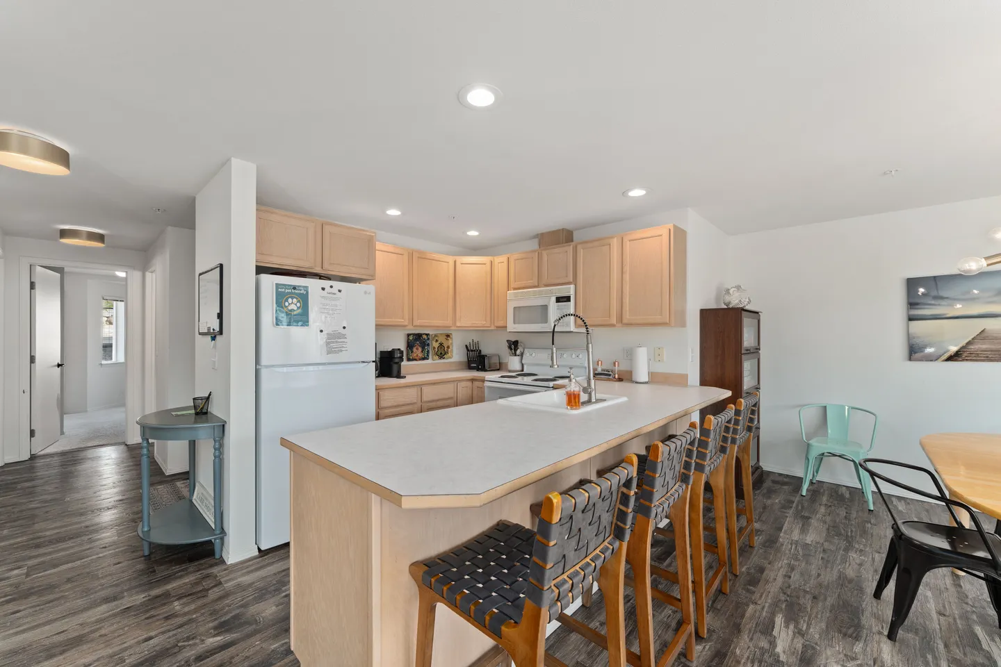 Open-concept kitchen with light wood cabinetry, white appliances, and a peninsula breakfast bar with barstools.