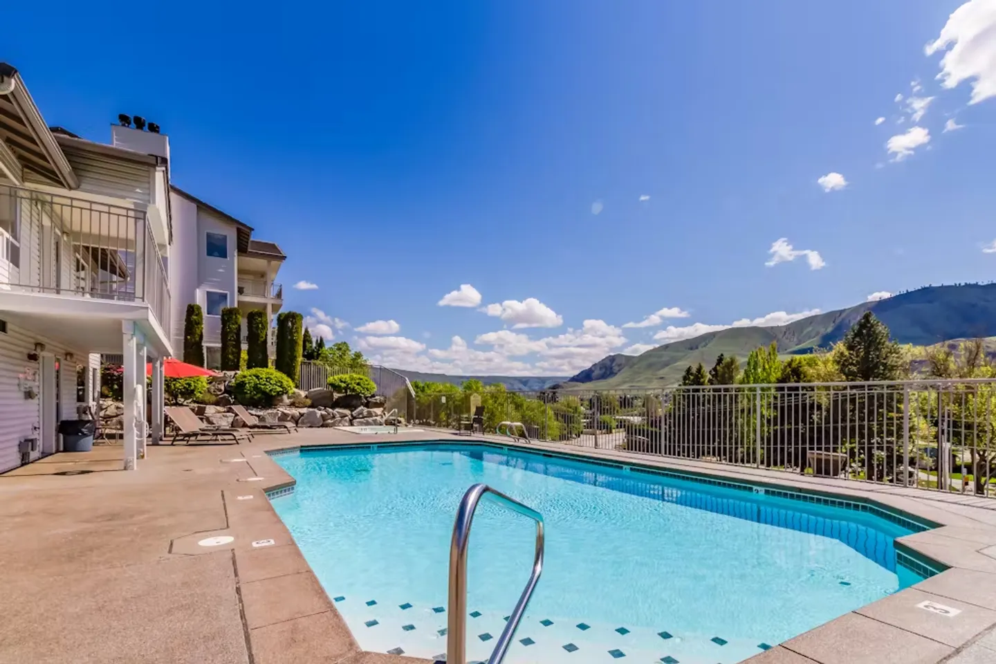 Outdoor swimming pool and patio area outside a multi-story building overlooking mountains.