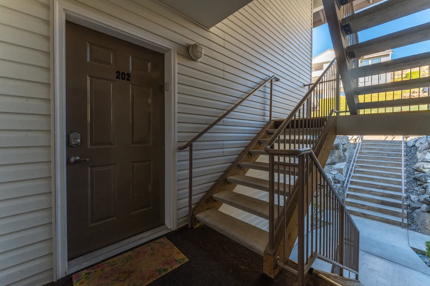 Exterior entrance area featuring unit door number 202 and an adjacent open staircase leading up.