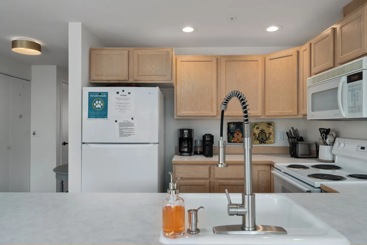 Kitchen counter view over a sink toward light wood cabinets, white appliances, and small countertop appliances.