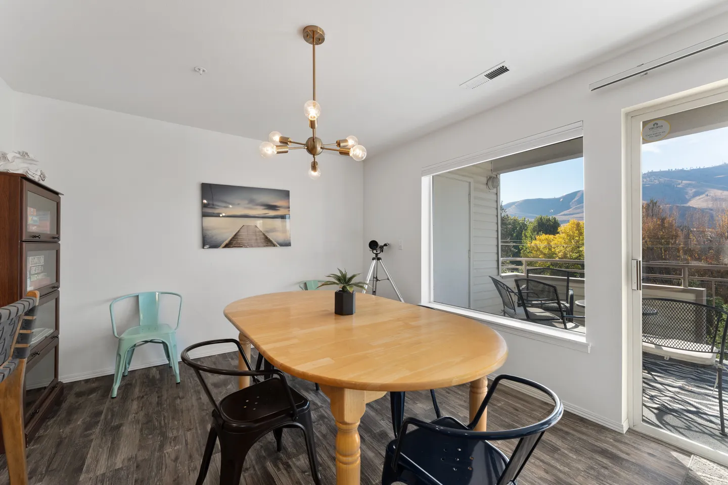 Dining area with an oval wood table, mixed metal chairs, and a picture window overlooking a balcony with mountain views.