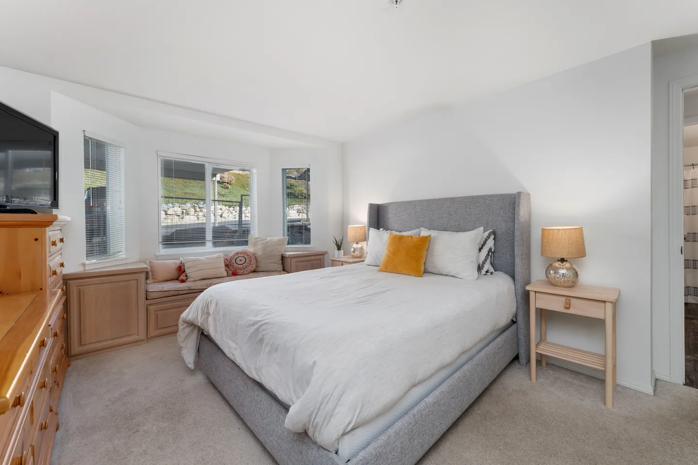 Bedroom featuring an upholstered bed, bay window with a cushioned window seat, and light wood furniture.