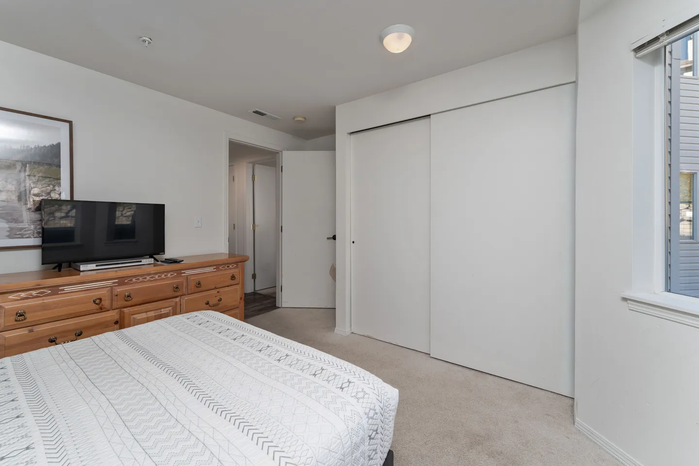 Bedroom featuring a patterned bed, a wooden dresser with a mounted TV, carpet flooring, and a large sliding closet door.
