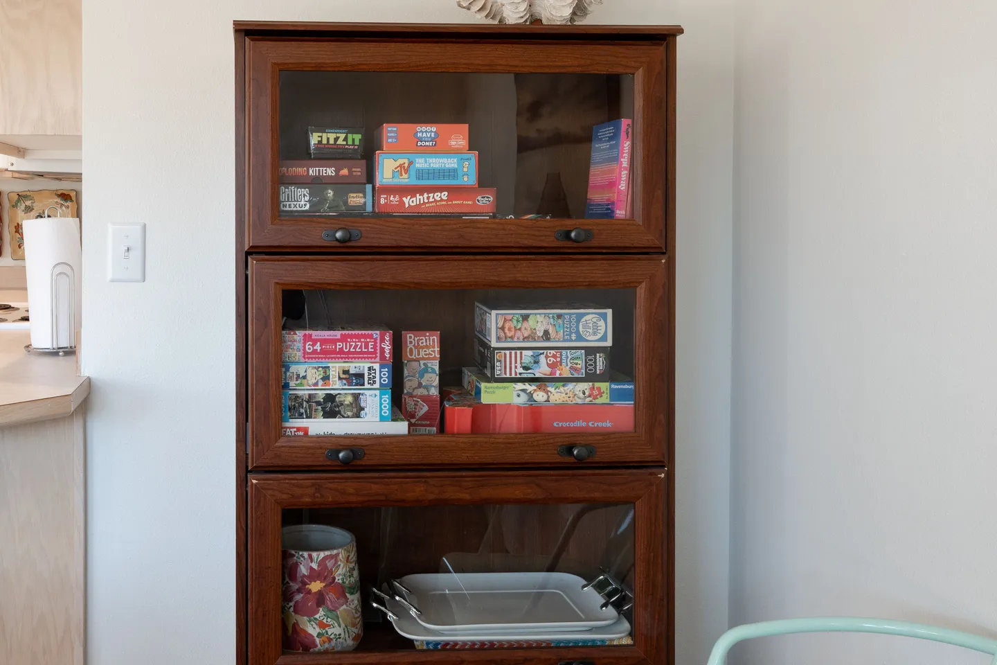 A wooden barrister cabinet with glass doors stocked with board games, puzzles, and serving trays.