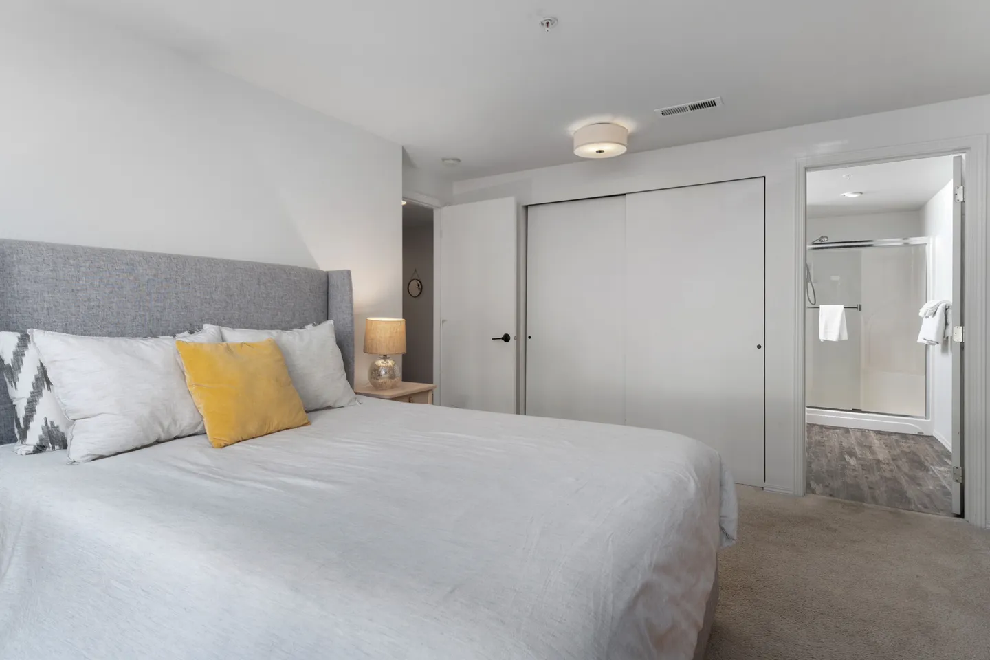 Bedroom with an upholstered gray bed, sliding closet doors, and an open doorway leading into an en suite bathroom.