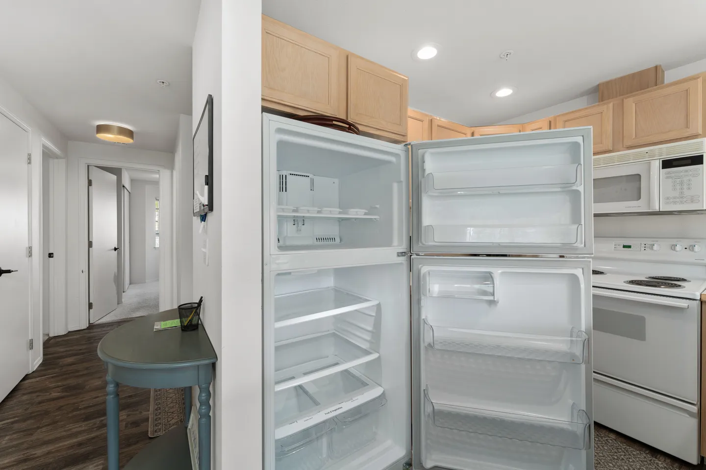 Open refrigerator and freezer in a kitchen next to a hallway and stove.