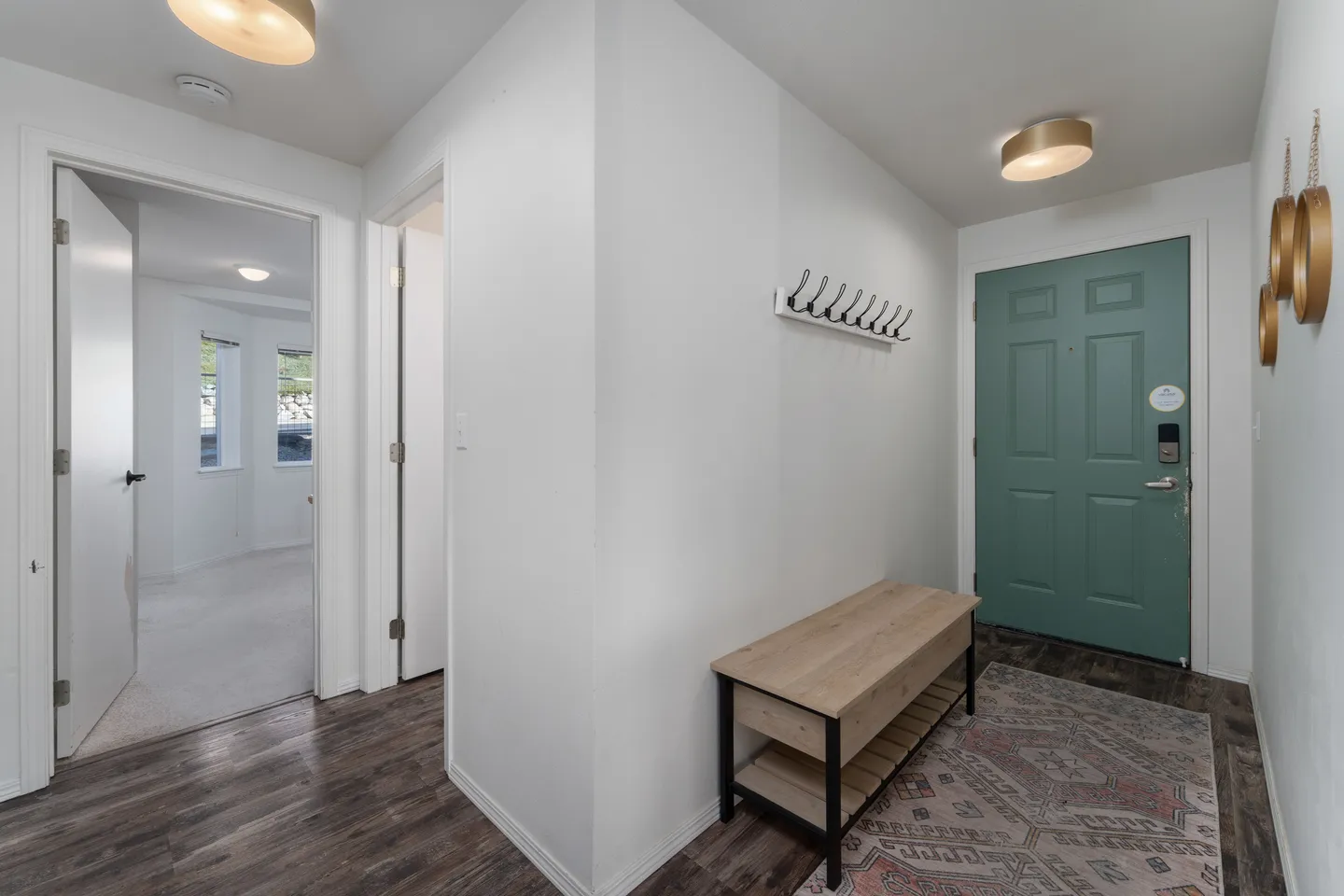 Entryway with a green front door, wooden bench, coat rack, and patterned area rug on dark wood-style flooring.