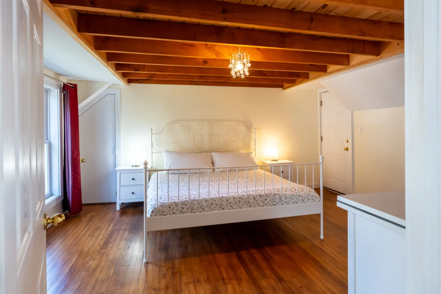 Bedroom with hardwood floors, exposed wood ceiling beams, and a white metal bed frame flanked by nightstands.