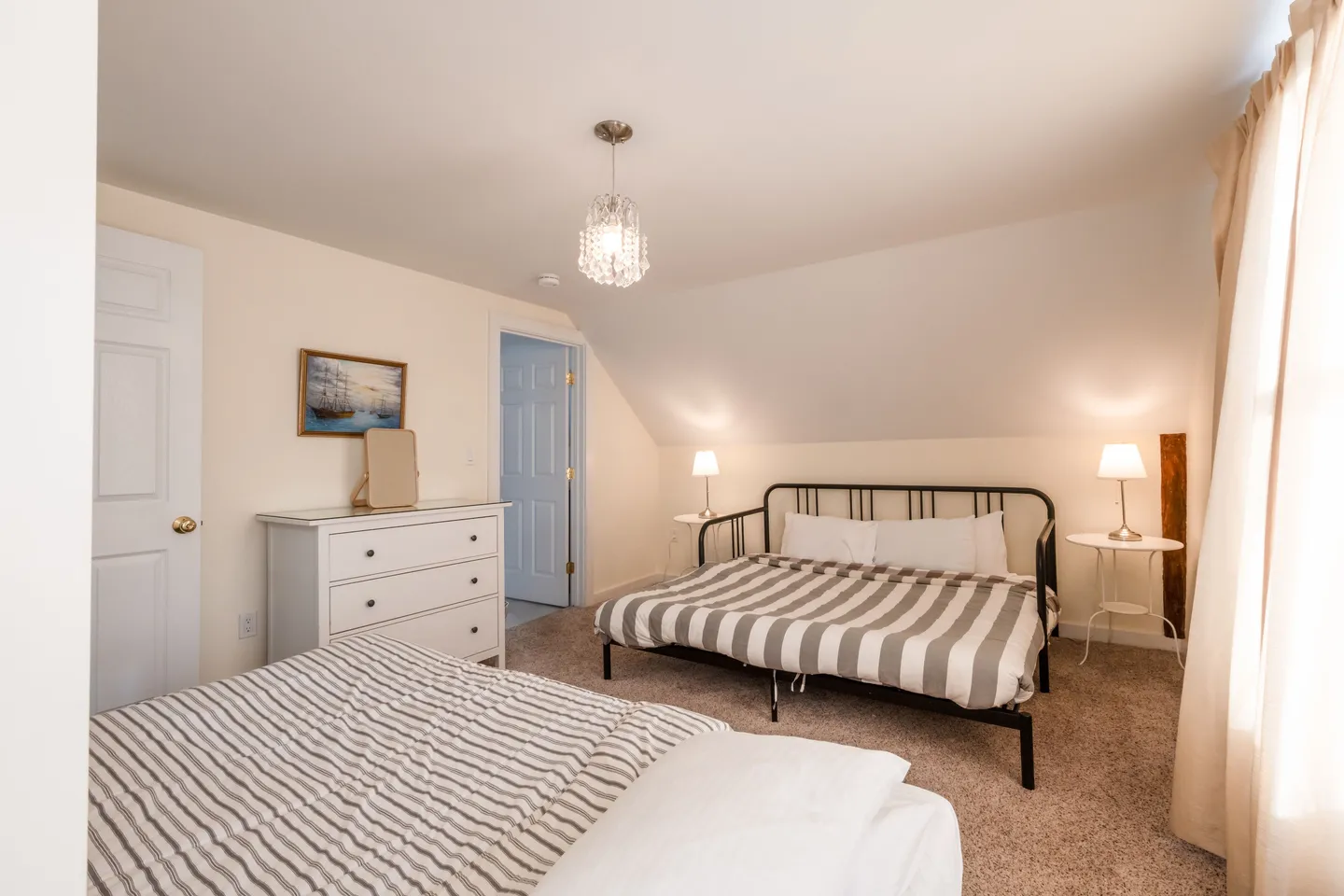 Bedroom with angled ceiling, two beds with striped bedding, a white dresser, and carpeted floor.