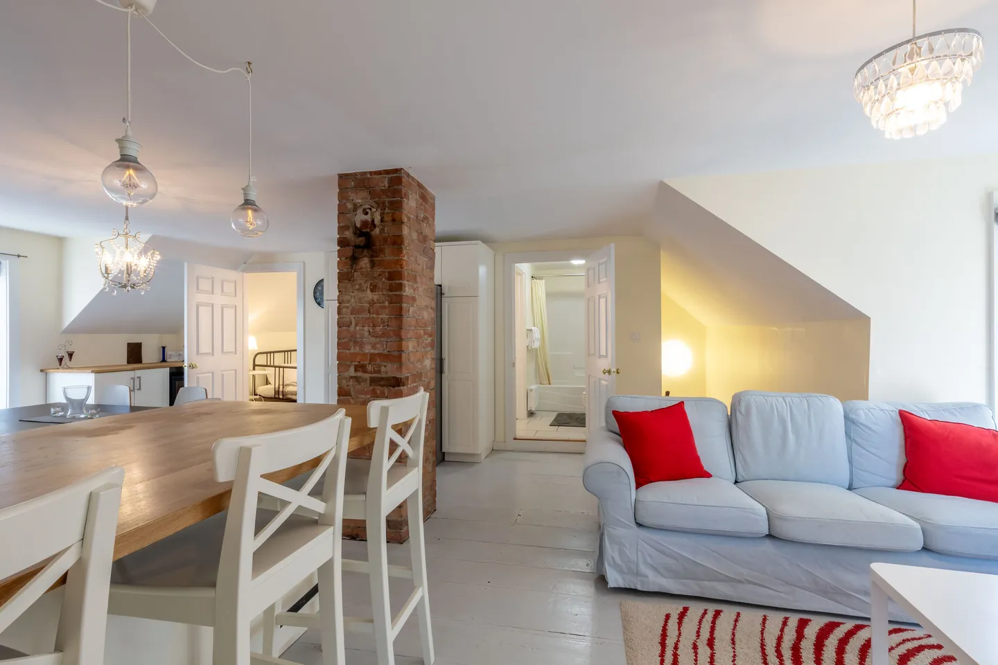 Open-concept living space with dining island, exposed brick pillar, sofa with red pillows, and views into adjacent rooms.