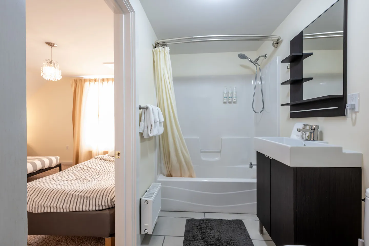 Bathroom with a bathtub shower combination, dark vanity, and an open doorway looking into a bedroom.