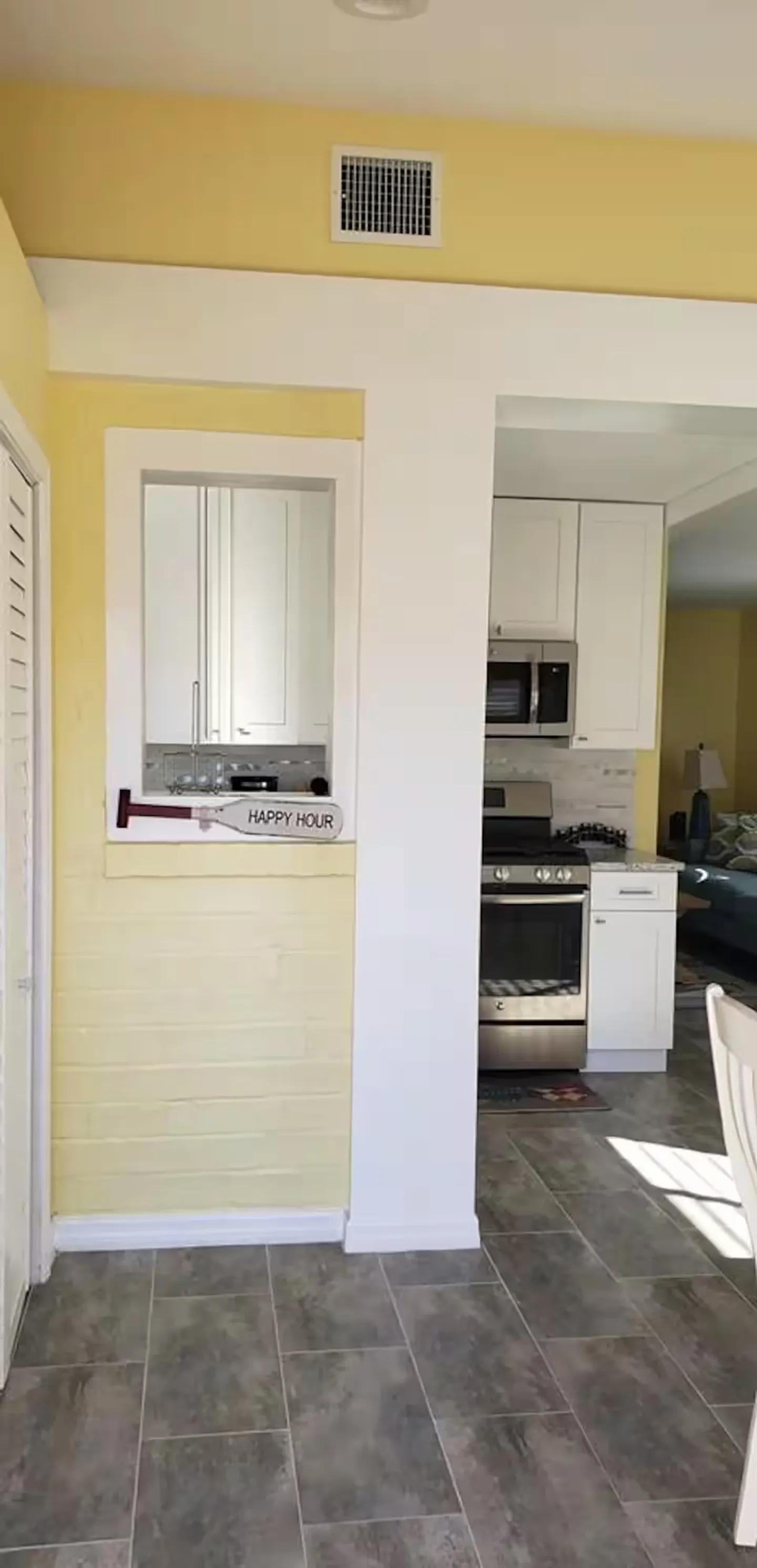 Pass-through window and doorway leading into a kitchen with stainless steel appliances and white cabinetry.