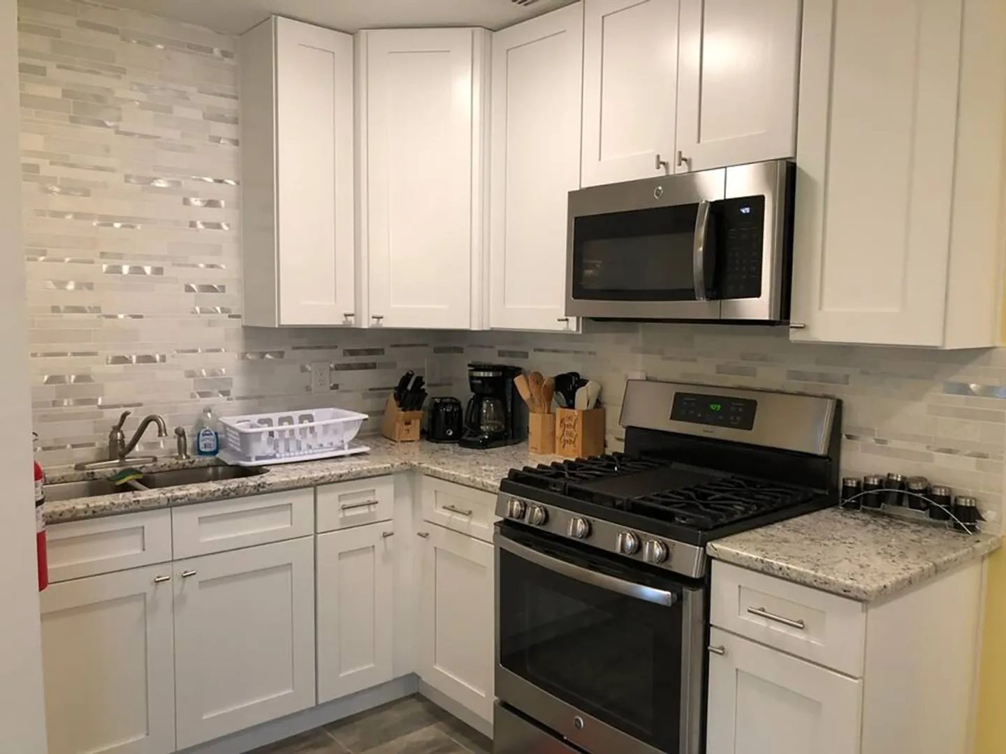 Kitchen corner featuring white shaker cabinets, light granite countertops, a gas range, over-the-range microwave, and a sink with tile backsplash.