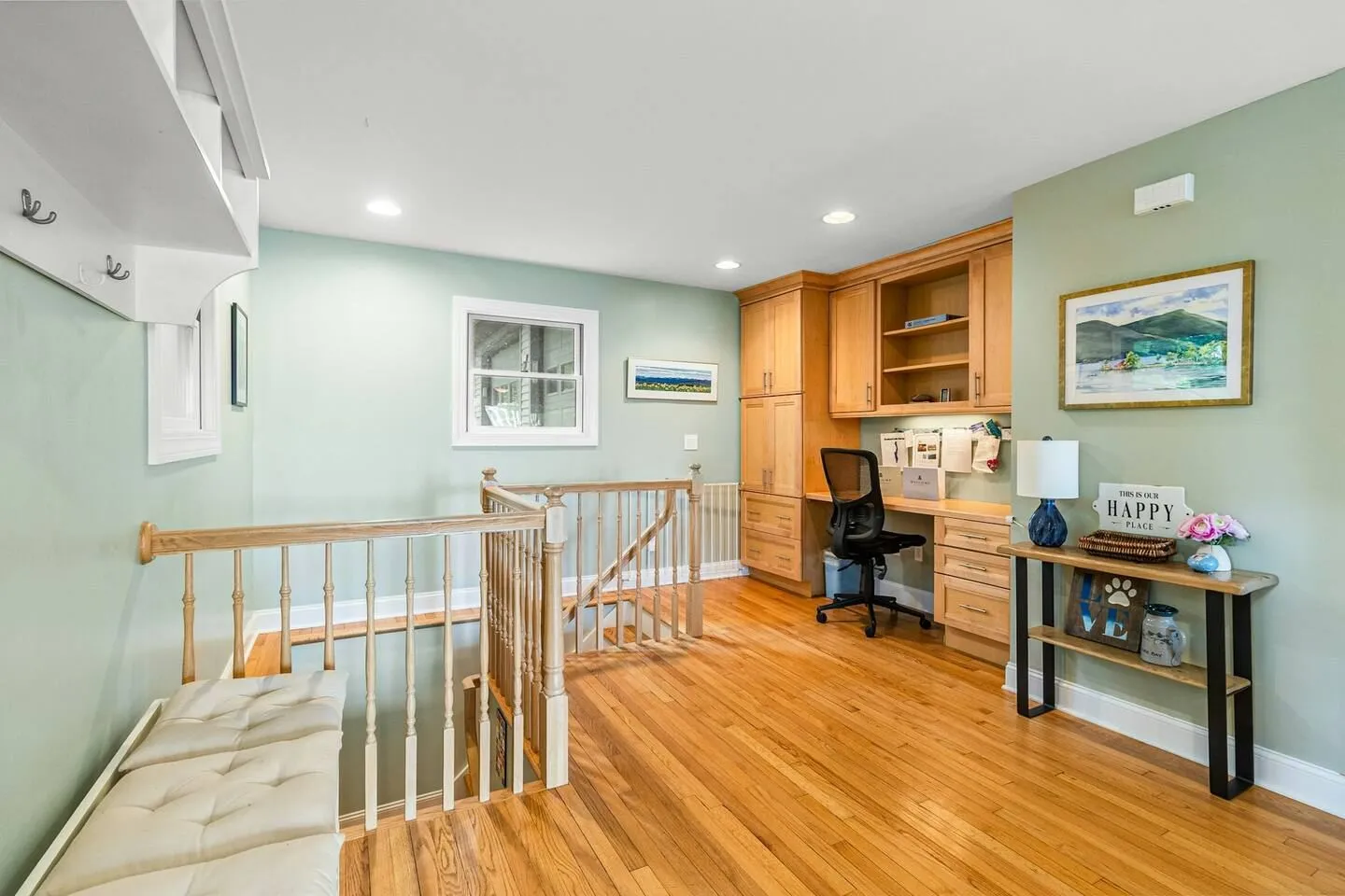Upstairs landing with hardwood floors, a staircase railing, a built-in wooden desk with an office chair, and a cushioned bench.
