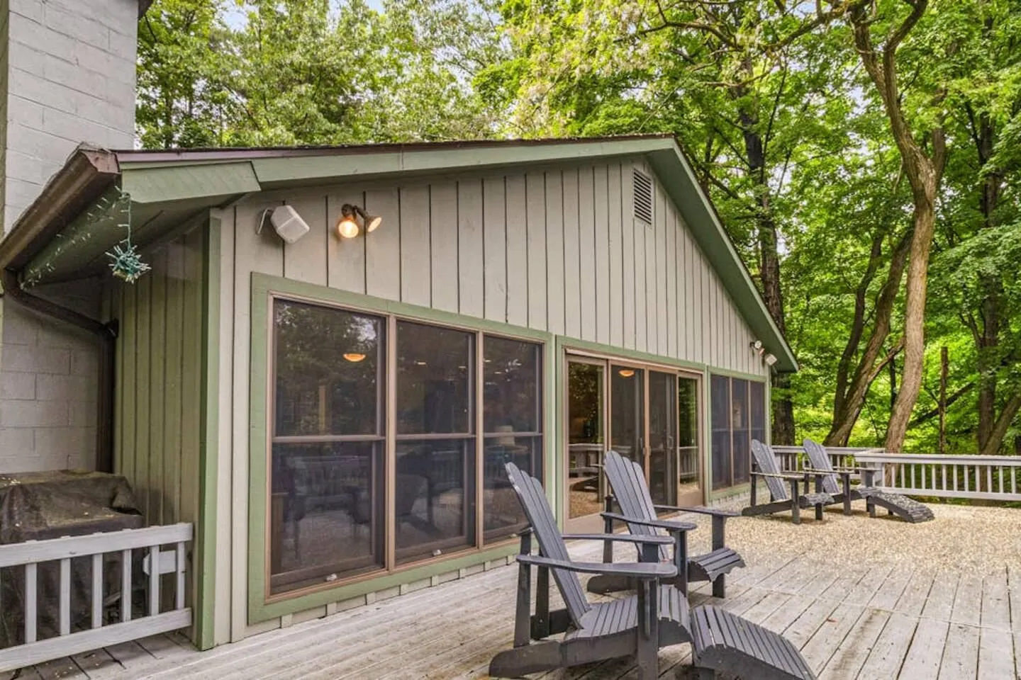 Exterior wooden deck with Adirondack chairs along the back of a house surrounded by trees.