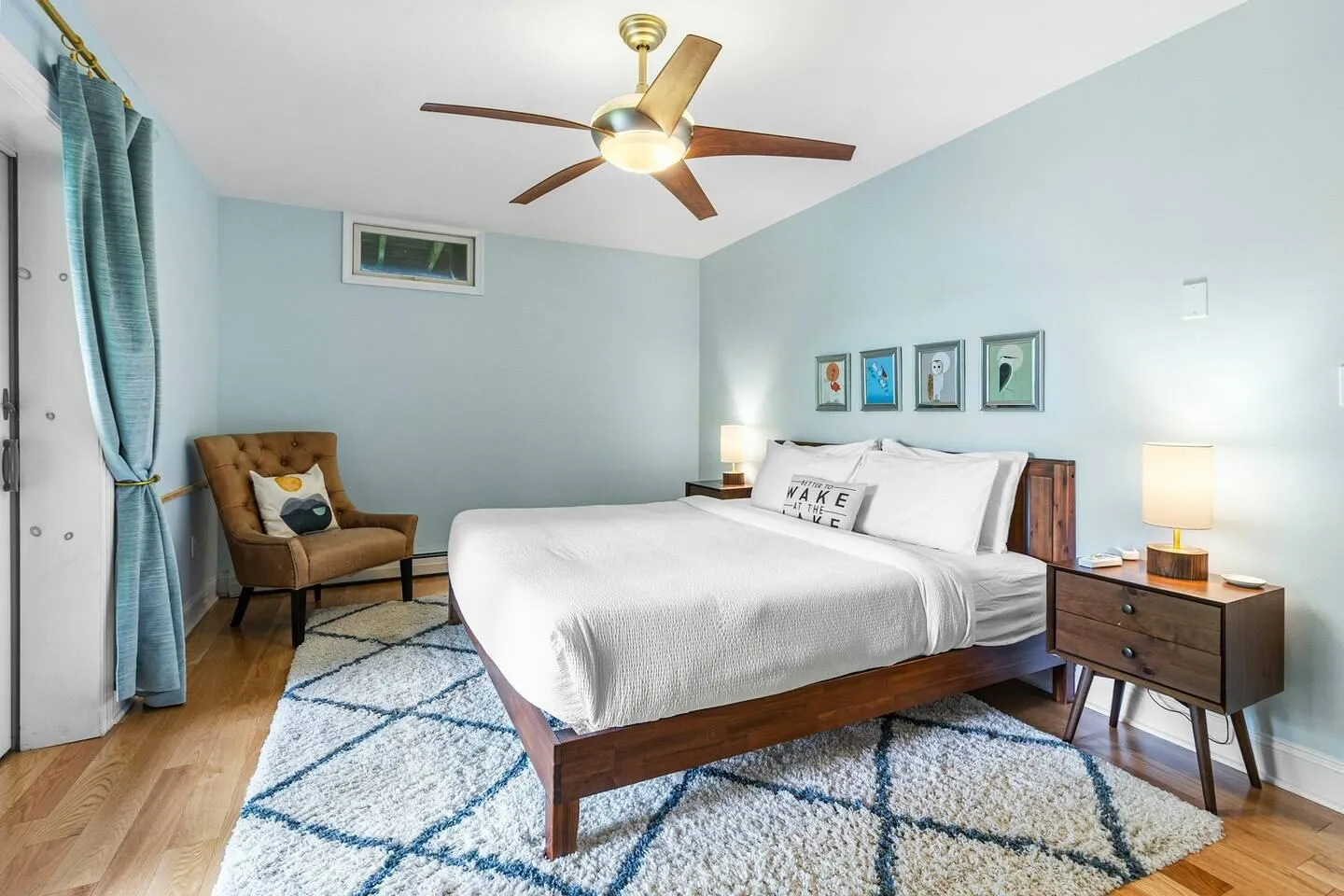 Bedroom with light blue walls, a wooden bed, patterned area rug, ceiling fan, and accent chair.
