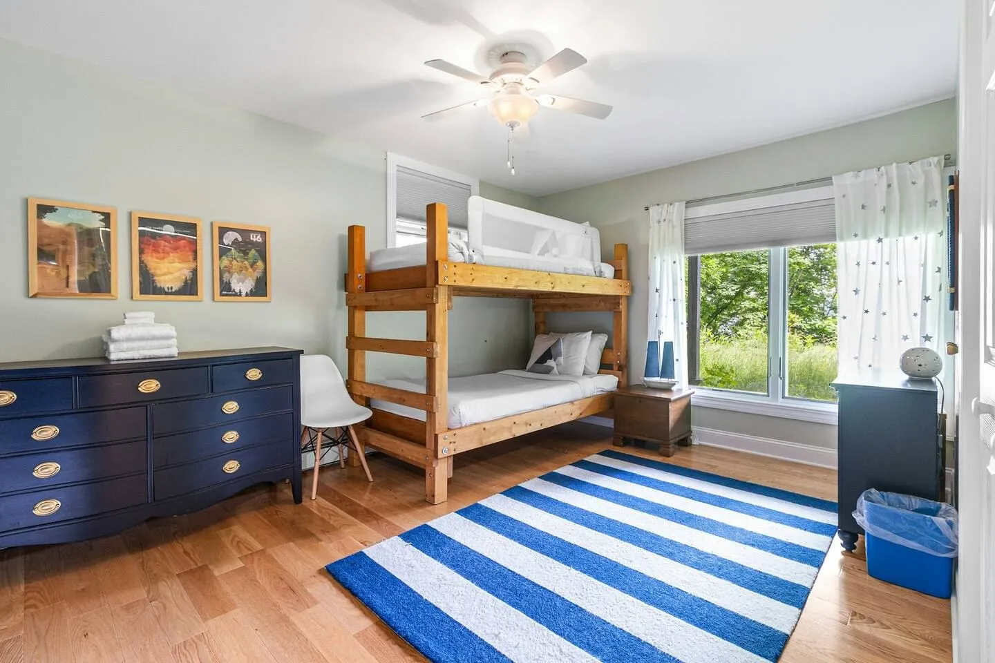 Bedroom with wooden bunk beds, a blue and white striped rug, a dark blue dresser, and light wood floors.