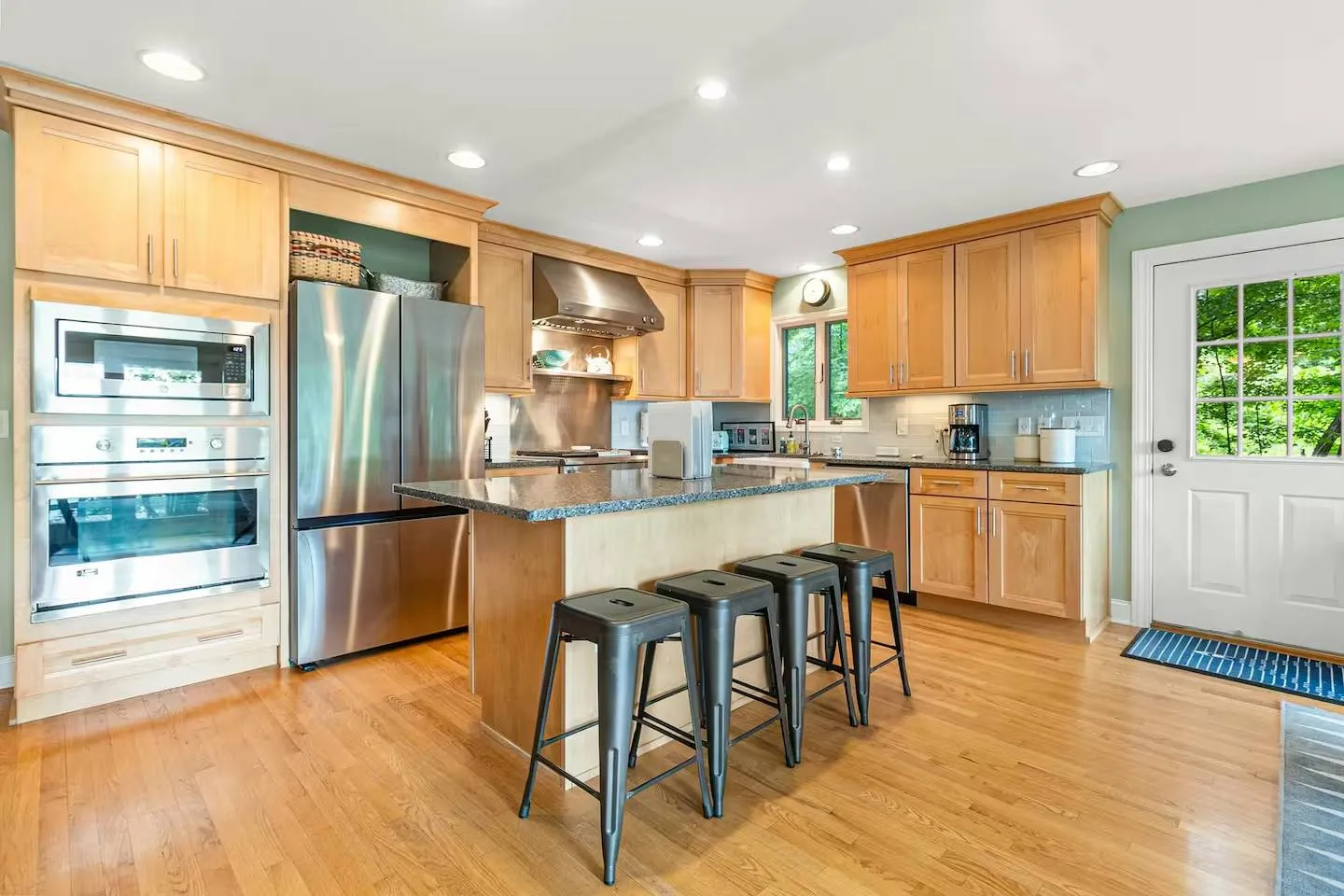 Kitchen with light wood cabinetry, stainless steel appliances, and a center island with four metal barstools.