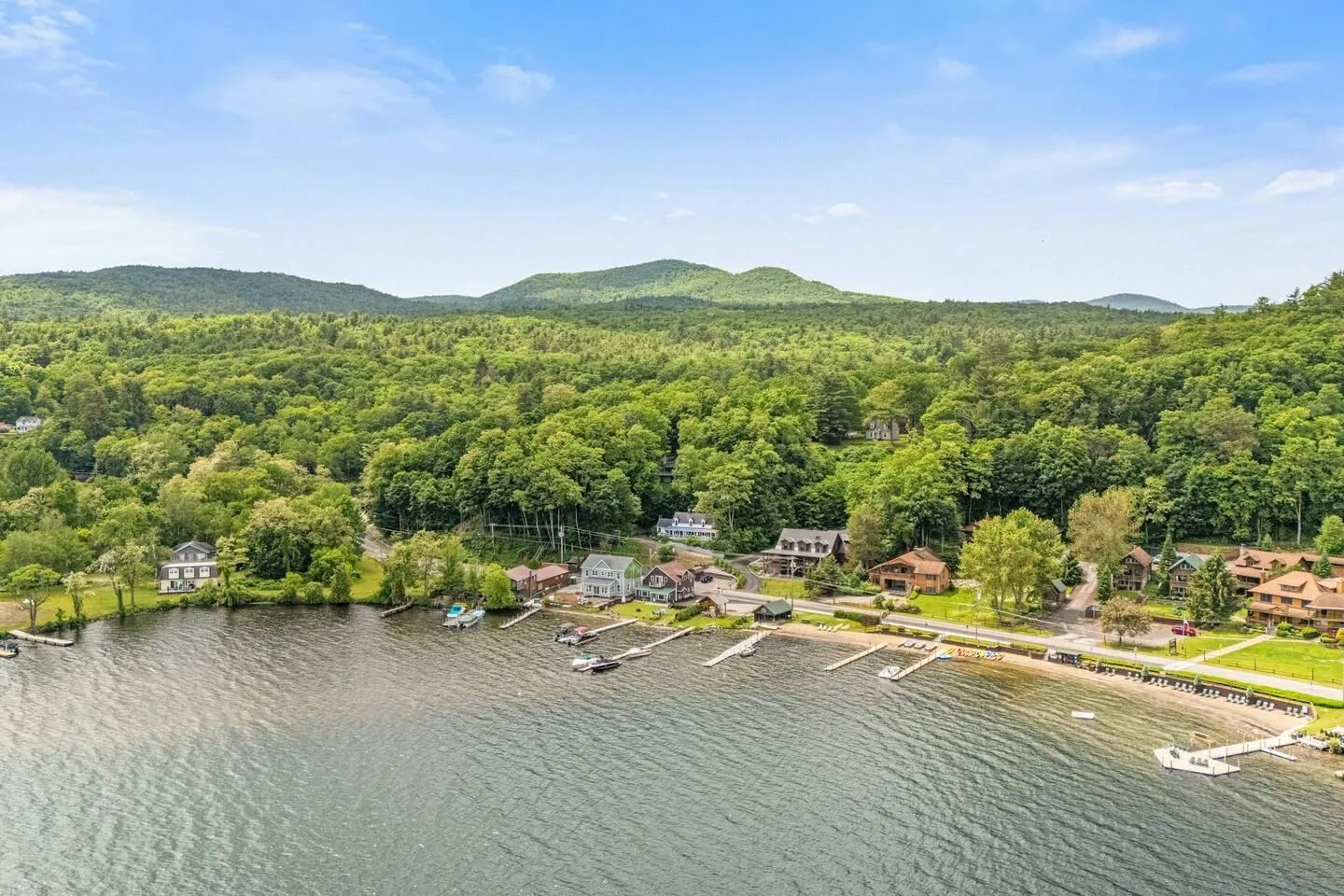 Aerial view of a lakefront shoreline with docks, houses, and densely forested hills in the background.