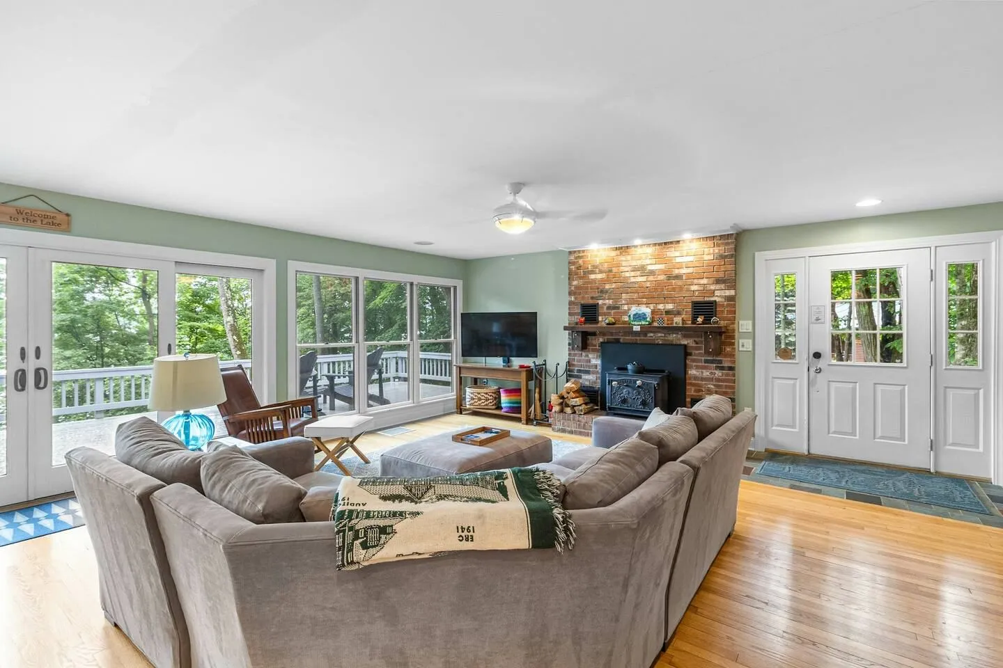 Living room with hardwood floors, a large sectional couch, a brick fireplace with a wood-burning stove insert, and sliding glass doors leading to a deck.