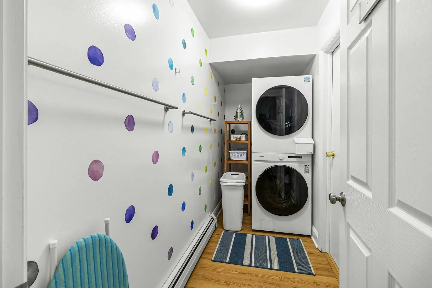 Laundry nook featuring stacked front-loading washer and dryer, polka-dot accent wall, and ironing board.