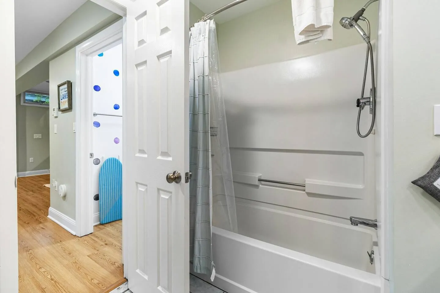 Bathroom with a white bathtub and shower combination next to an open doorway leading to a hallway.