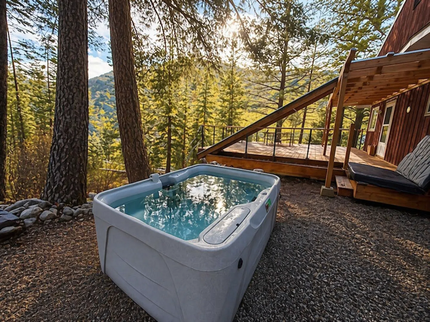 Outdoor hot tub filled with clear water next to a raised wooden deck with mountain and forest views.