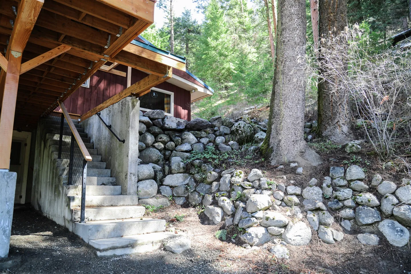 Exterior concrete stairs leading up to a red cabin with rock retaining walls and pine trees.