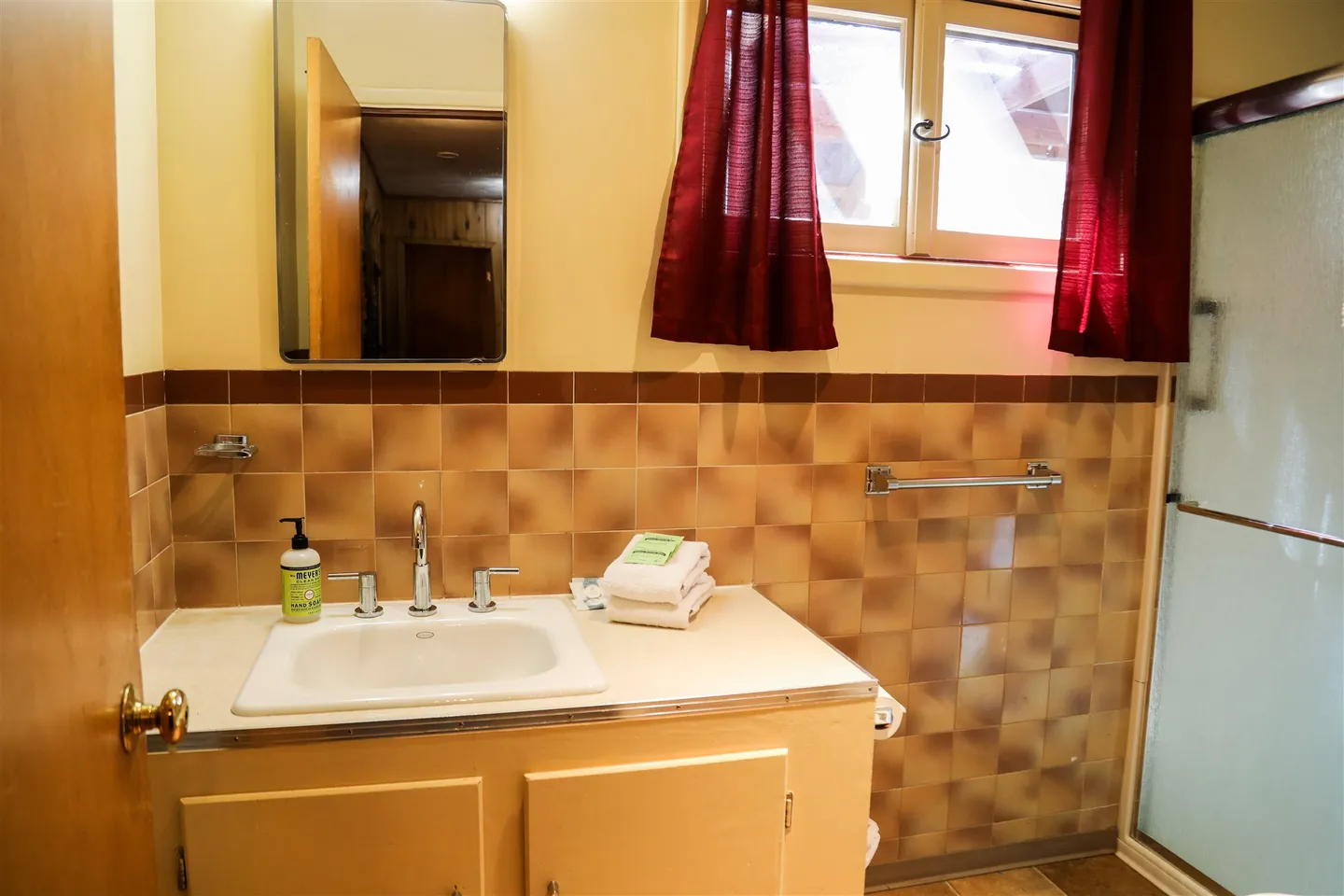 Bathroom featuring a vanity with a white drop-in sink, brown checkered tile backsplash, a mirror, and a frosted glass shower door.
