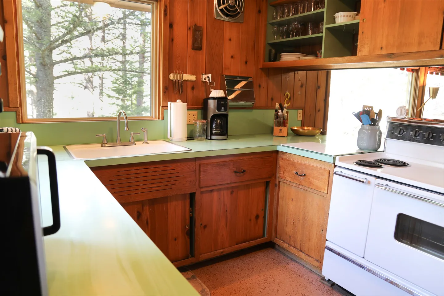 Kitchen with wood-paneled walls and cabinets, mint green countertops, a white sink under a window, and a white electric range.