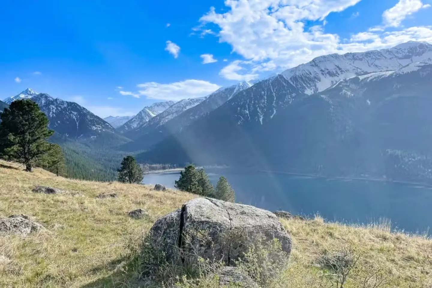 Elevated scenic view of a lake bordered by rugged mountains under a blue sky with scattered clouds.