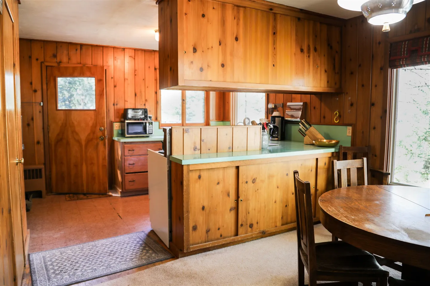 Rustic kitchen and dining area featuring knotty pine wood-paneled walls and cabinetry with green countertops.
