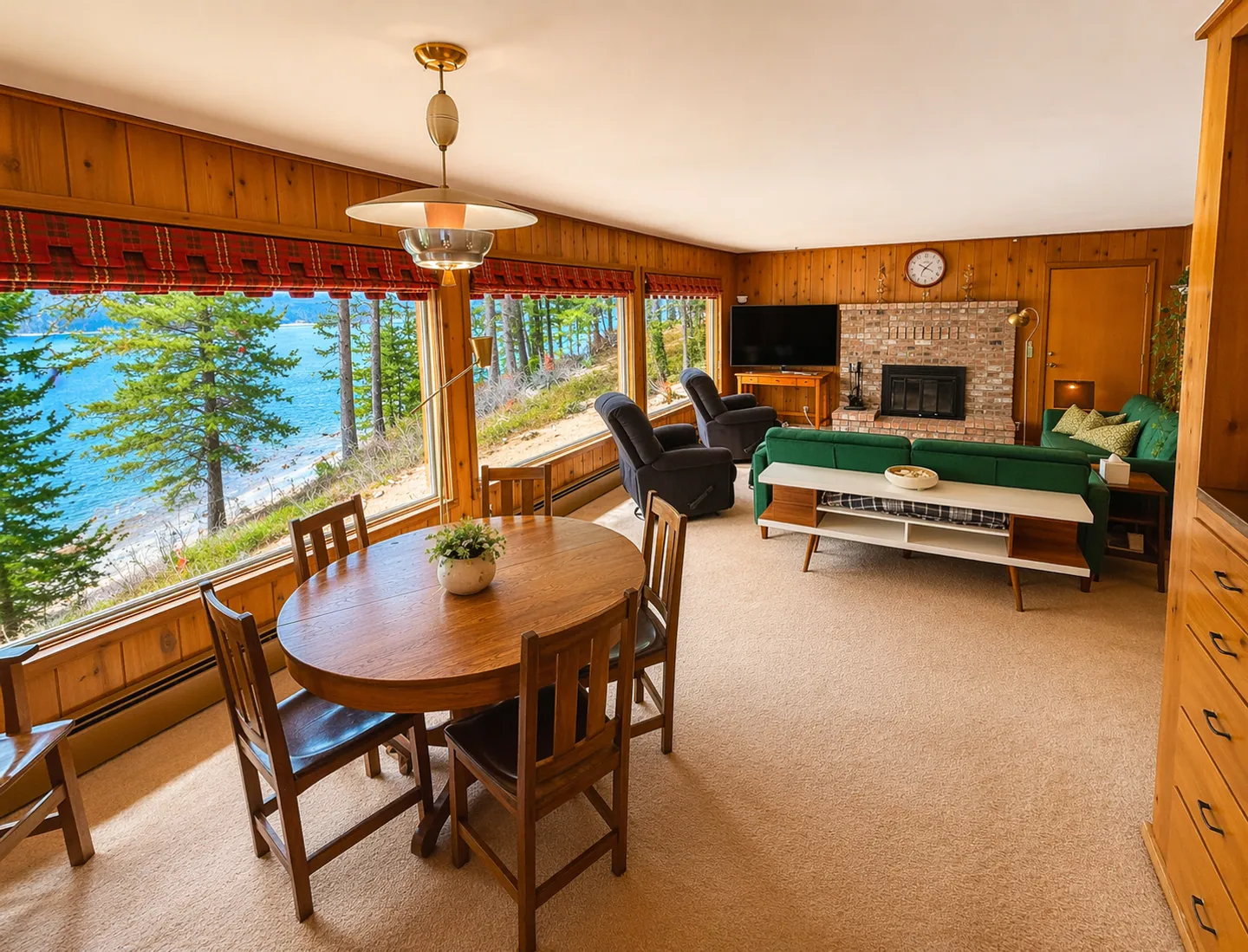 Open living and dining area with wood-paneled walls, carpeted floors, and expansive windows offering a water view.