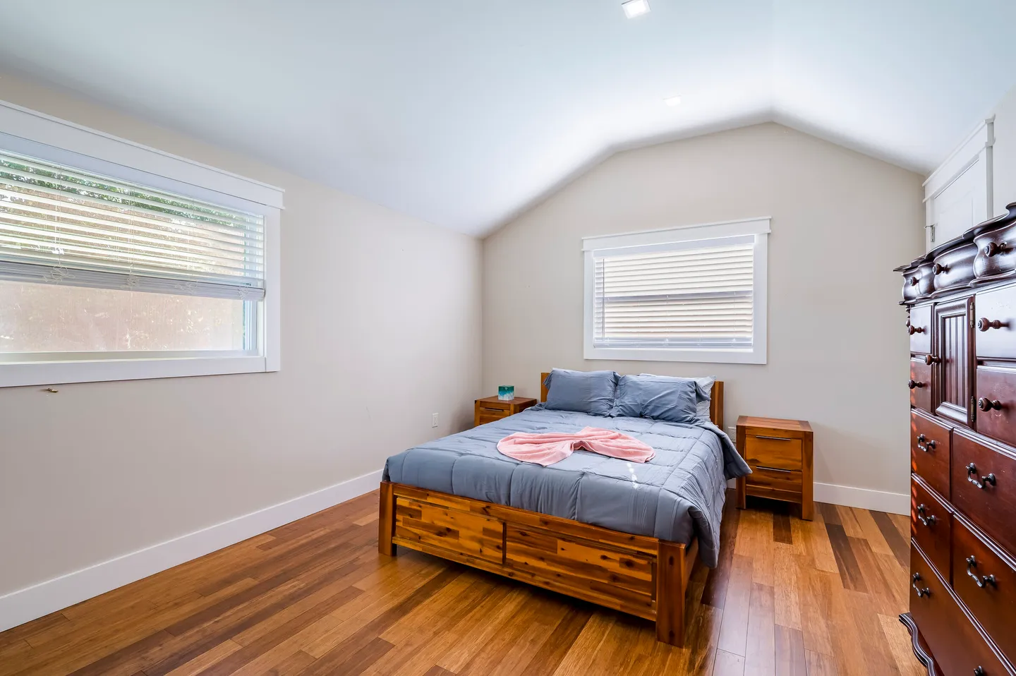Bedroom with wood-look flooring, a vaulted ceiling, a wooden bed frame, two matching nightstands, and a tall wooden dresser.