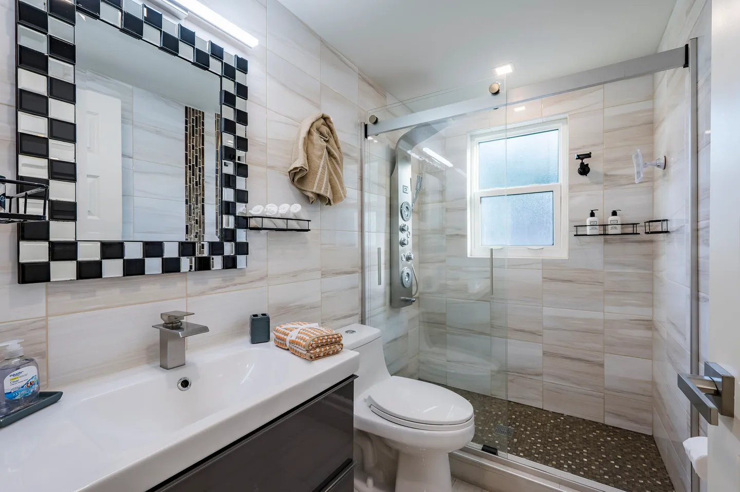 Modern bathroom featuring a vanity with a checkered mirror, a toilet, and a glass-enclosed shower with tiled walls.