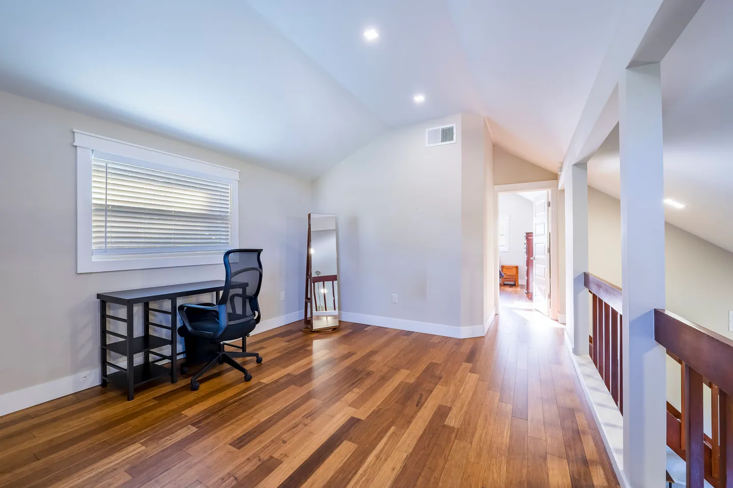 Upstairs landing with wood flooring featuring a small desk with an office chair, a freestanding mirror, and a railing looking over the lower level.