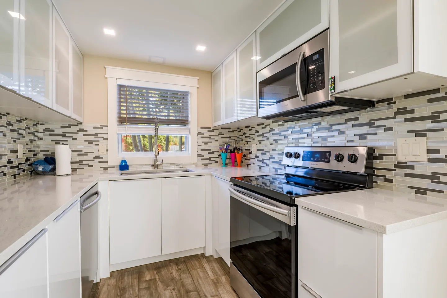 Modern U-shaped kitchen with white cabinetry, light quartz-style countertops, stainless steel appliances, and a mosaic tile backsplash.