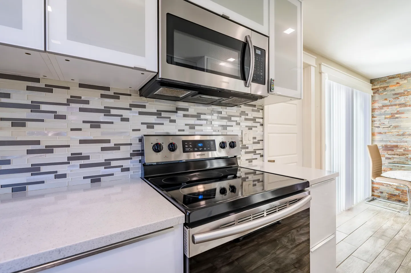 Close-up view of a stainless steel microwave and electric stove in a kitchen with white countertops and a mosaic tile backsplash.