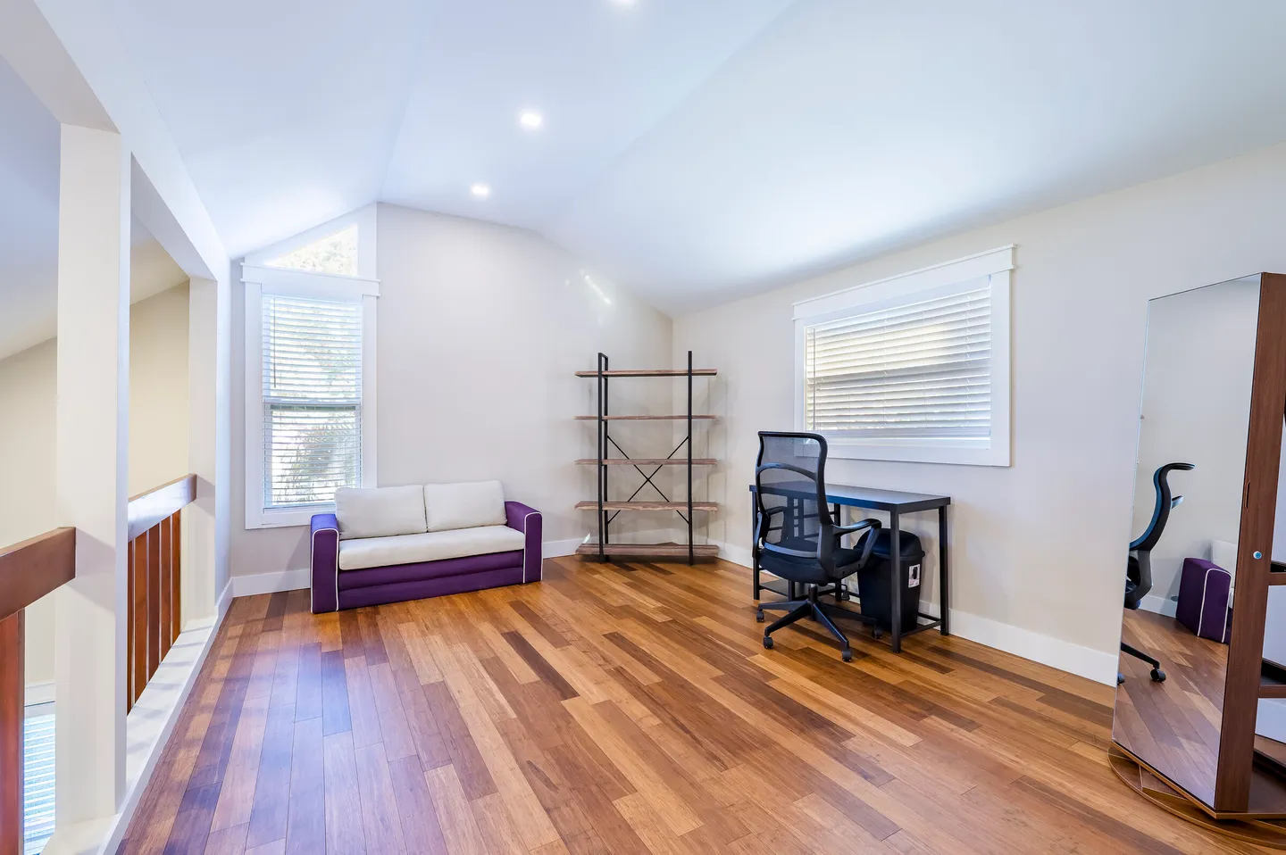 Upstairs loft space with wood-look floors, a desk and office chair, an open bookshelf, a small sofa, and a standing full-length mirror.