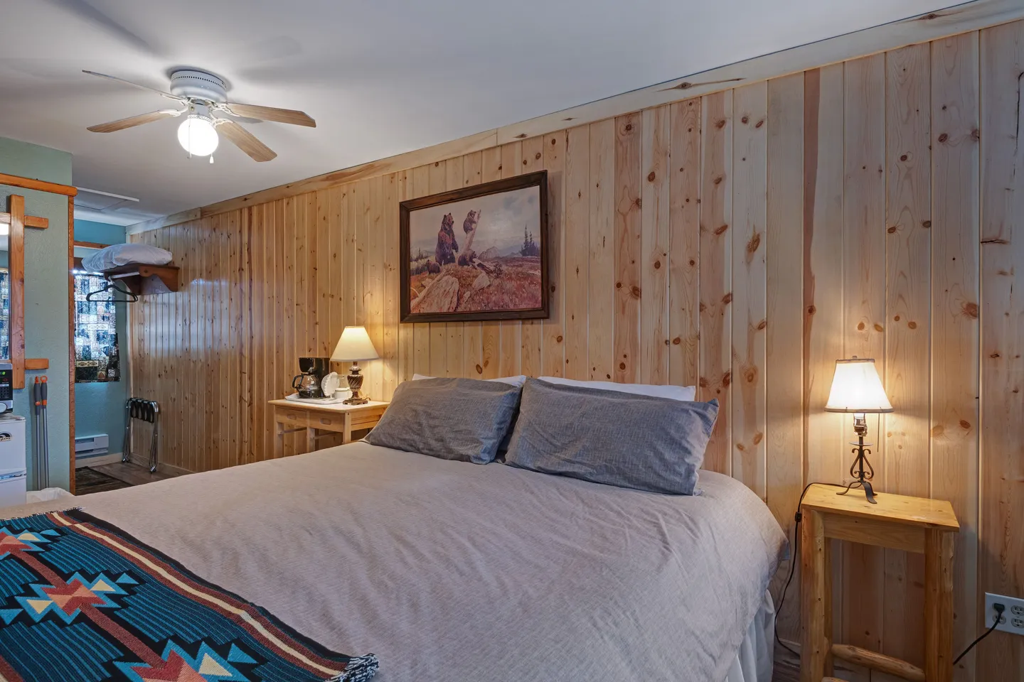 Bedroom featuring wood-paneled walls, a made bed, nightstands with lamps, a ceiling fan, and framed wildlife art.