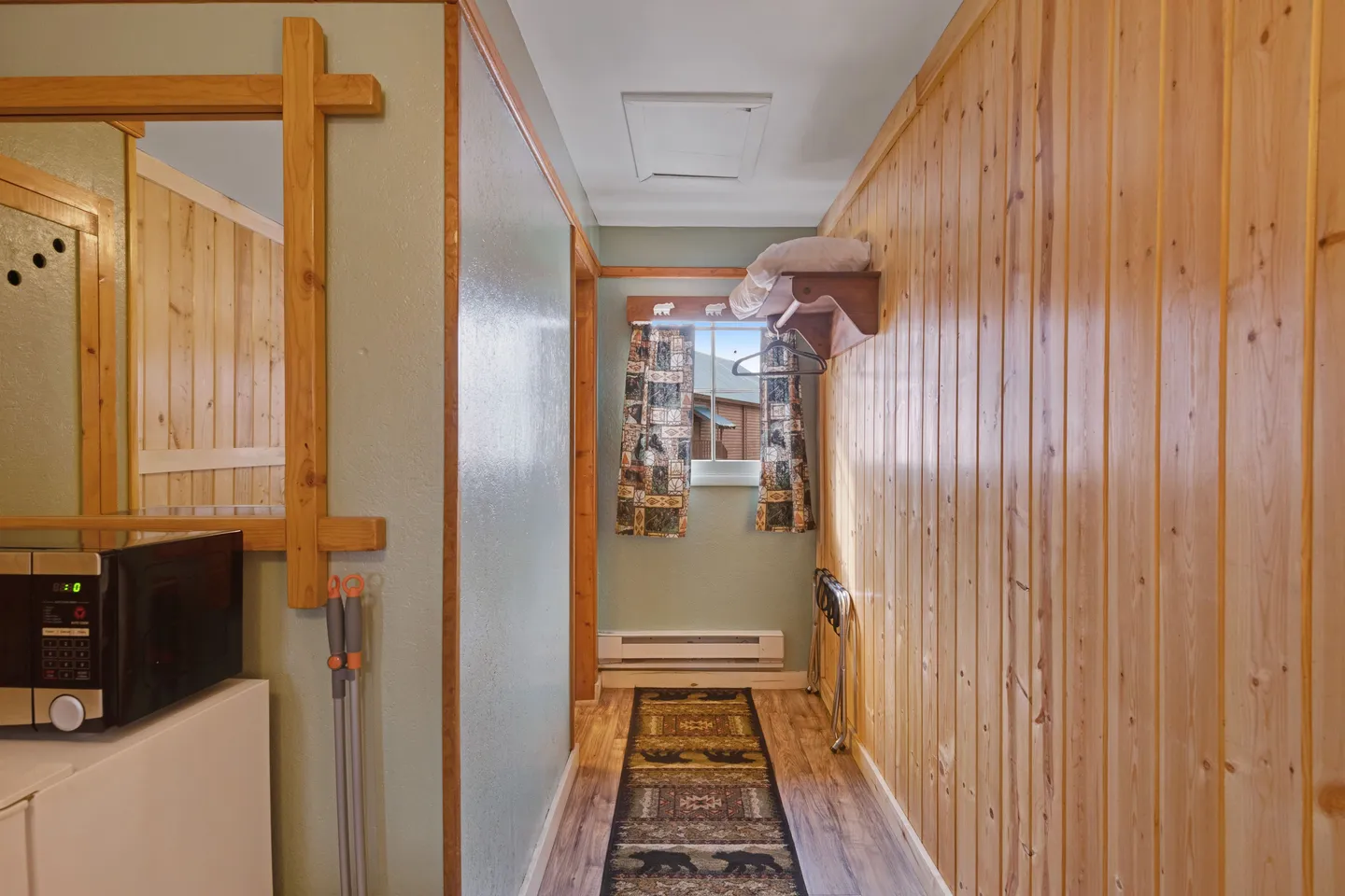Hallway featuring wood-paneled walls, a runner rug, and a small window at the far end.
