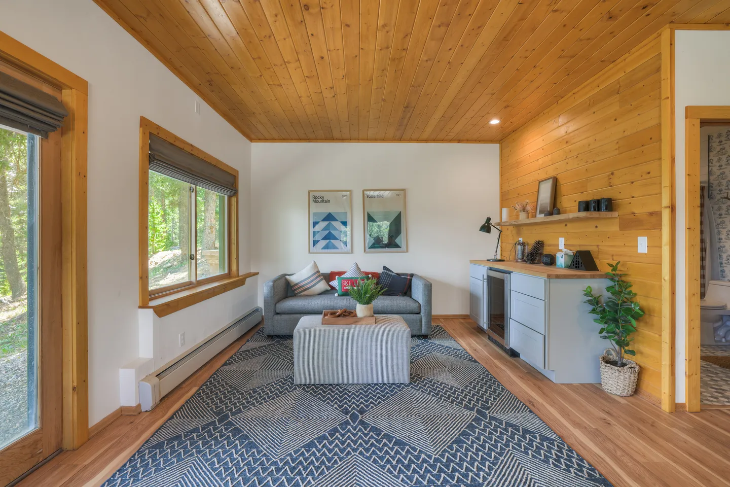 A sitting area featuring wood-paneled ceilings, a small sofa, an ottoman, a patterned blue rug, and a mini bar counter with a beverage fridge.